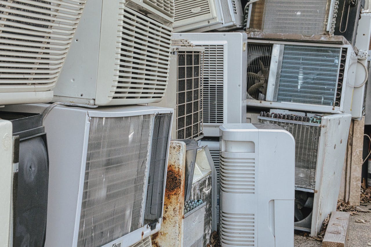 Home A collection of various old and broken air conditioning units piled outdoors.