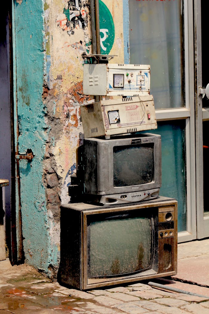 about-me Old, dusty TVs stacked against a weathered wall on a Delhi street, showcasing urban decay.
