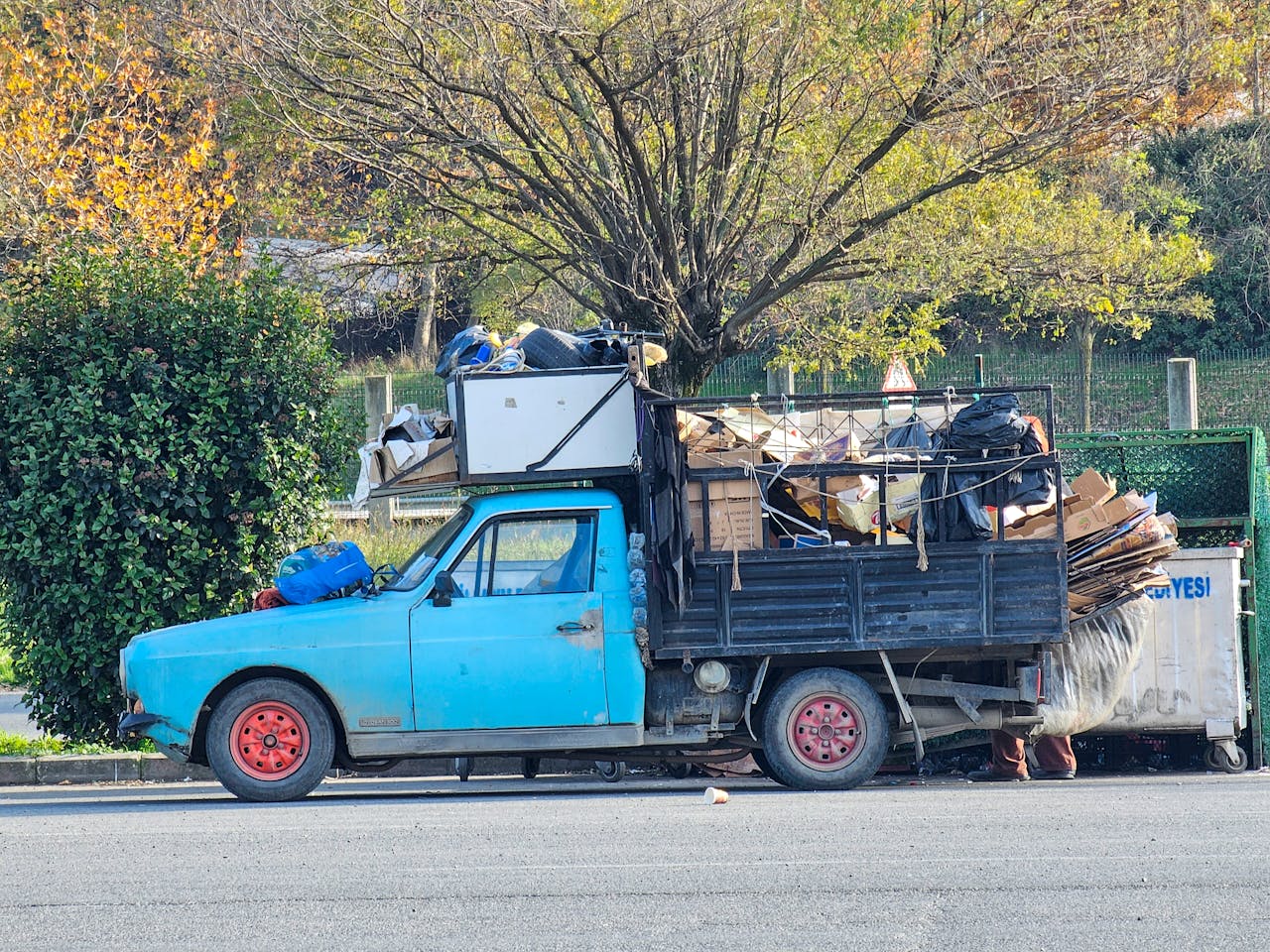 Home Side view of a vintage blue truck loaded with recyclable waste on a sunny day.