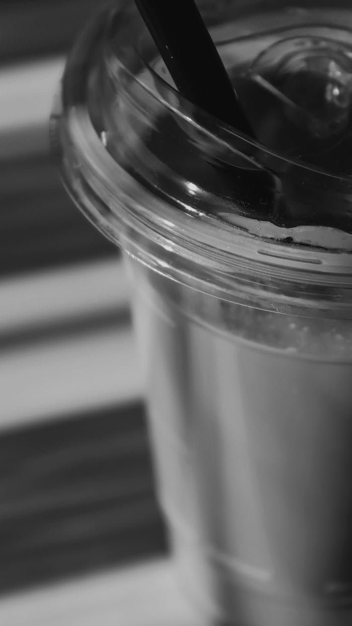 Services Black and white close-up of a plastic cup with straw on a striped background.